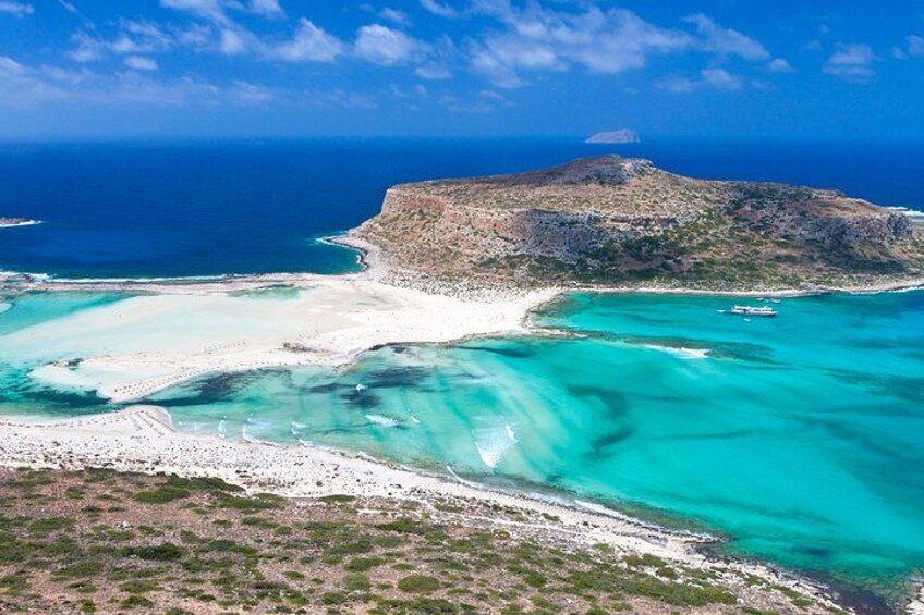 A coastal landscape with a prominent rocky island, clear turquoise waters, and a sandy beach. 3