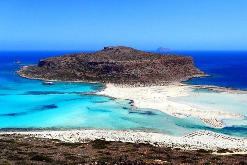 A coastal landscape with a rocky island, clear turquoise waters, and a sandy beach. 2