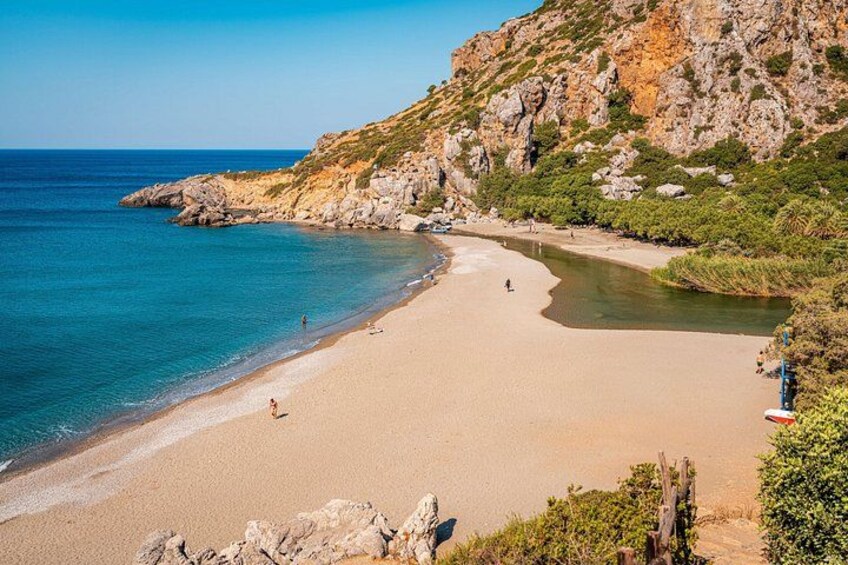 A beach with clear blue water, sandy shore, rocky cliffs, and sparse vegetation. 1