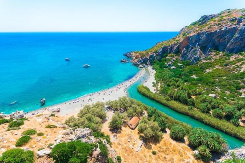 A coastal landscape with a beach, clear blue sea, rocky cliffs, and lush greenery. 1