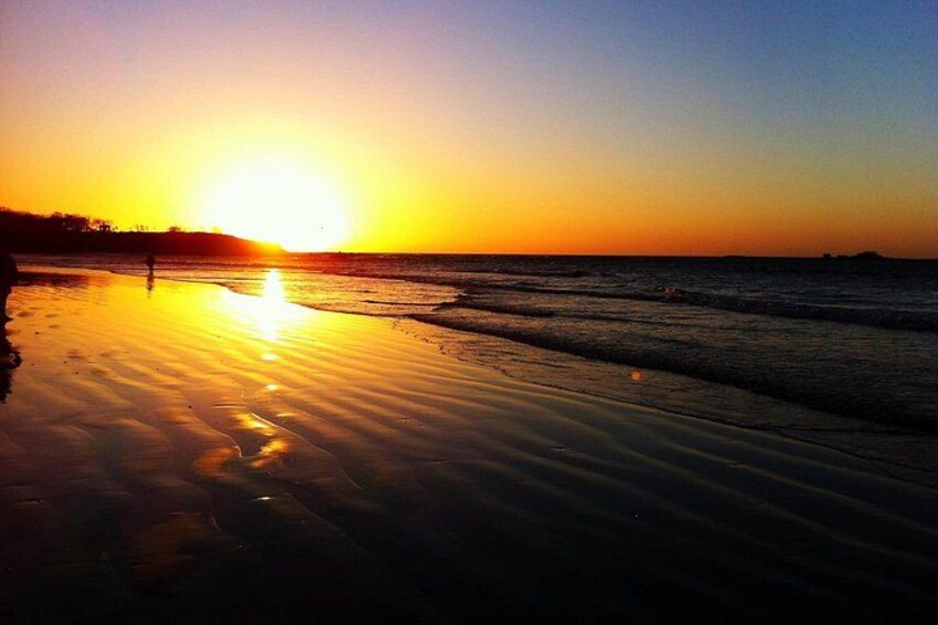 Un atardecer sobre una playa con aguas tranquilas que reflejan el cielo. 3