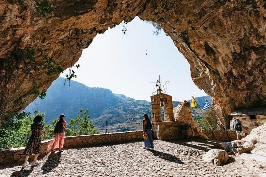 Entrada rocosa a una cueva con vistas a montañas, una torre pequeña e una bandera. 2
