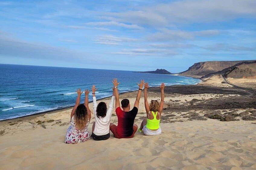 Four people sitting on a sandy beach with their backs to the camera, facing the ocean. 5