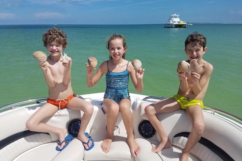 Drei Kinder in einem Boot, die Muscheln halten, mit einem Schiff im Hintergrund. 5