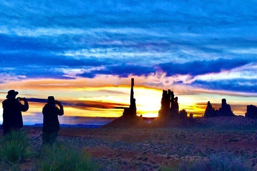 Un coucher de soleil sur un paysage désertique, avec des formations rocheuses et des personnes prenant des photos. 1