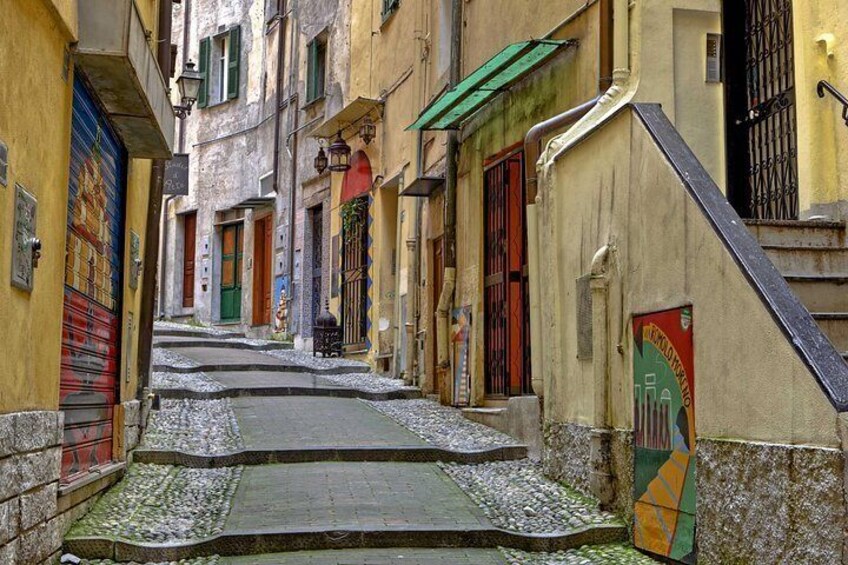 Una calle estrecha con pavimento adoquinado, puertas coloridas y una escalera que lleva a un edificio. 2