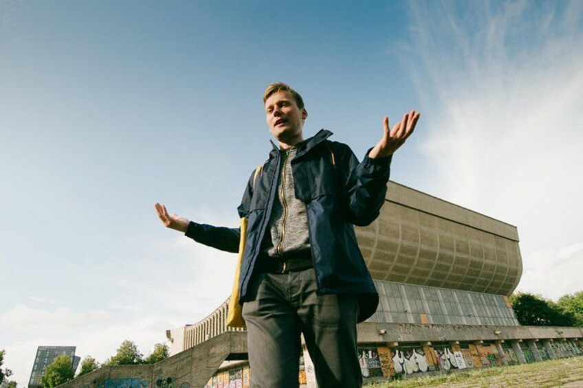 A person standing with arms outstretched in front of a modern building with graffiti. 3