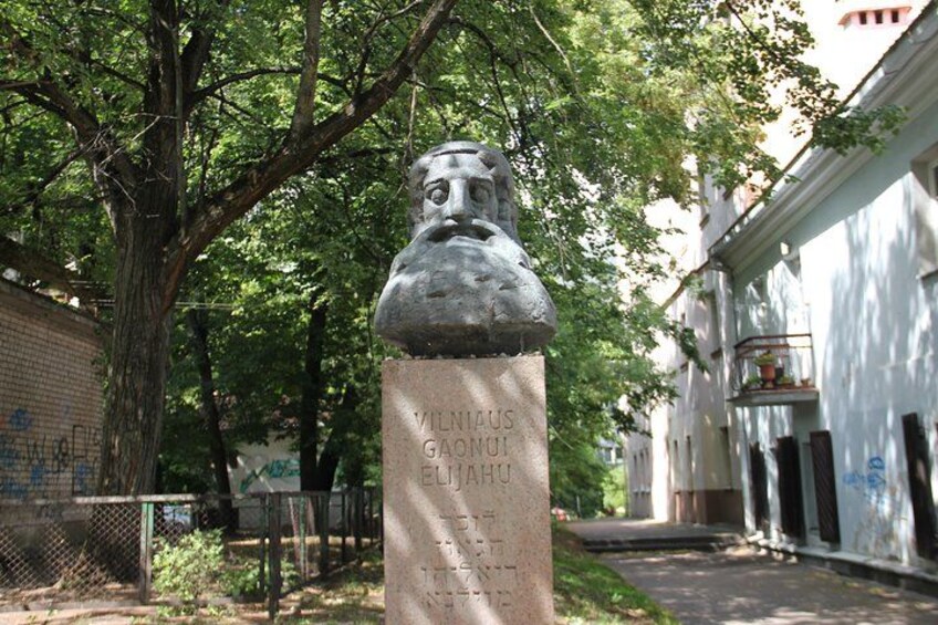 En staty av en man med skägg och mustasch, placerad på en sockel med en plakett. 2