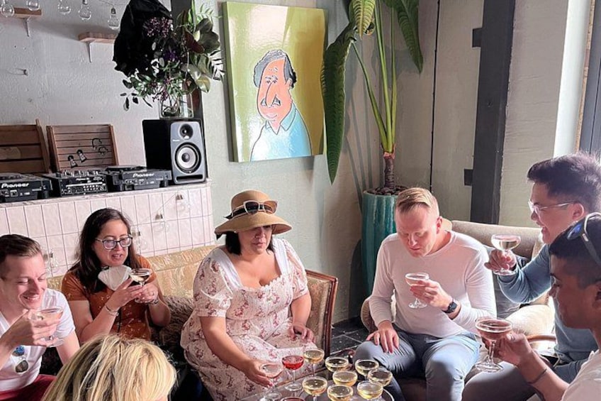 Un groupe de personnes est assis autour d’une table, des boissons sont posées devant elles, dans une pièce où l’on aperçoit un haut-parleur et un tableau accroché au mur. 2