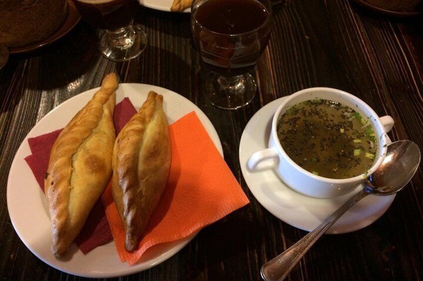 A plate with two pastries, a cup of soup, and a spoon on a table. 2