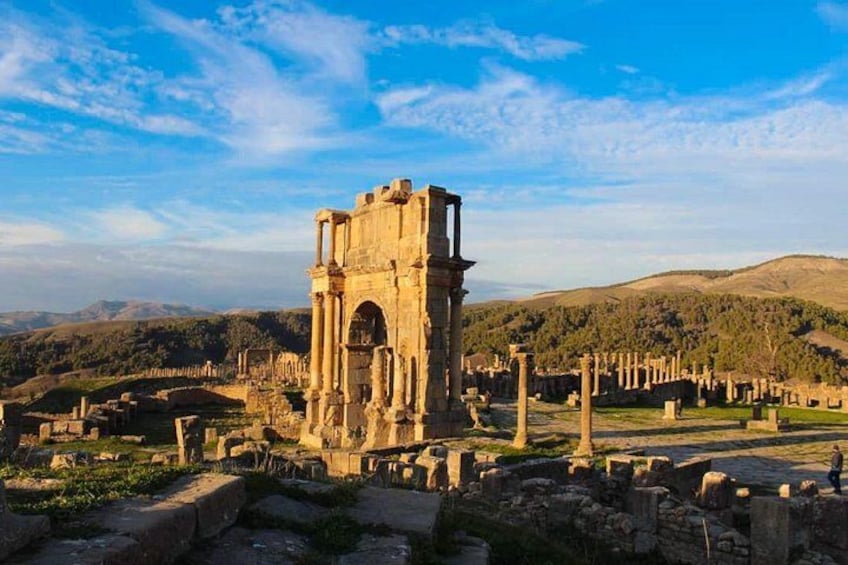 Ancient ruins with columns and arches, set against a backdrop of hills and a clear sky. 4