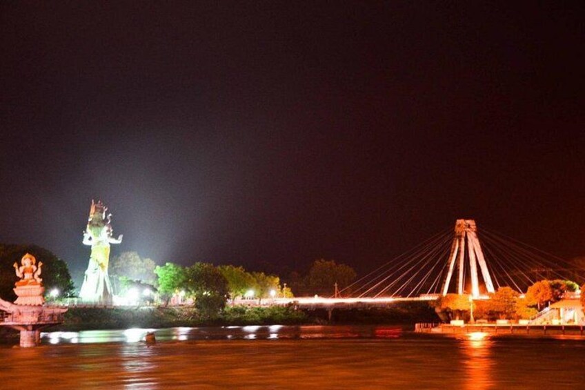 A night scene with a lit-up statue and a cable-stayed bridge over a body of water. 2