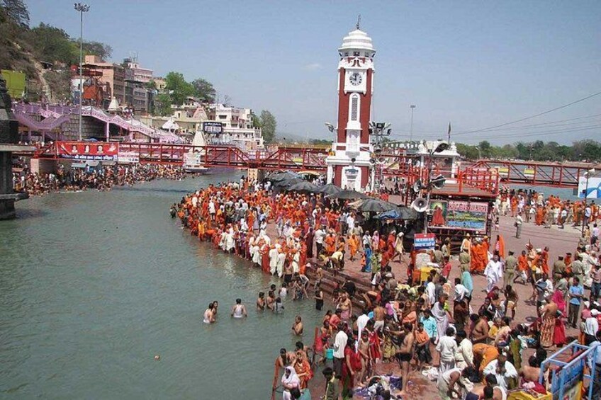 A crowded riverside with a clock tower and a bridge. 2