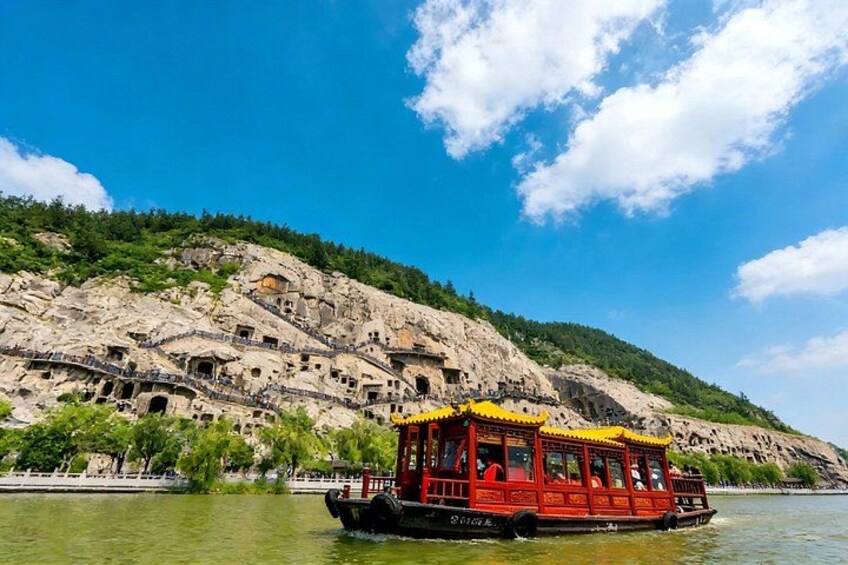 Ein Boot auf einem Fluss, eine felsige Klippe mit alten Bauwerken und ein klarer, blauer Himmel. 1