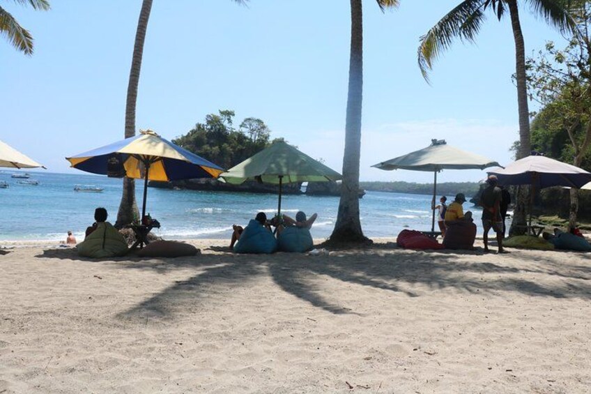 A beach with people sitting under umbrellas, palm trees, and the ocean. 3