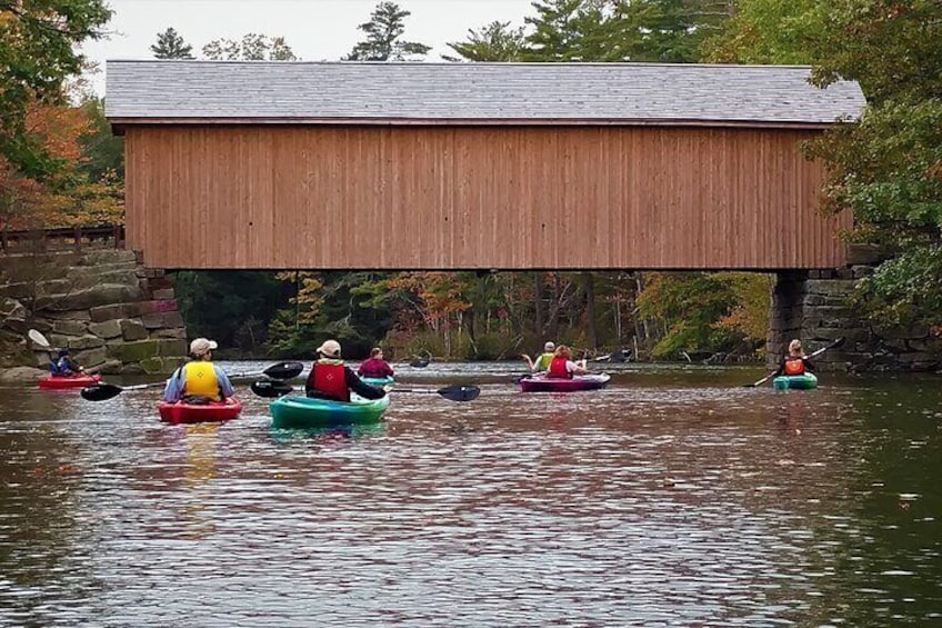 People kayaking on a river under a wooden bridge. 1