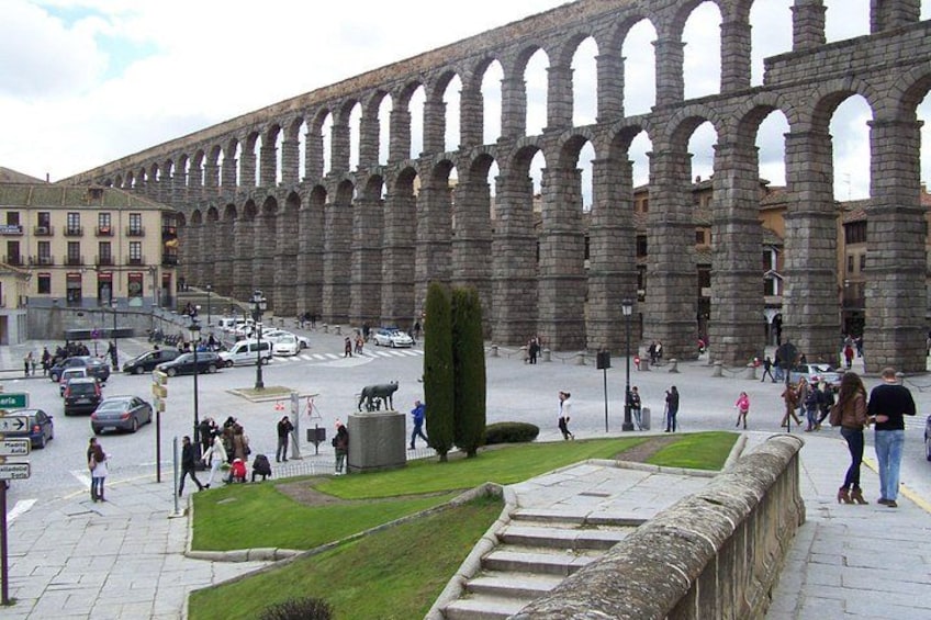 A large stone aqueduct with arches, a grassy area, and a statue of a bull. 3