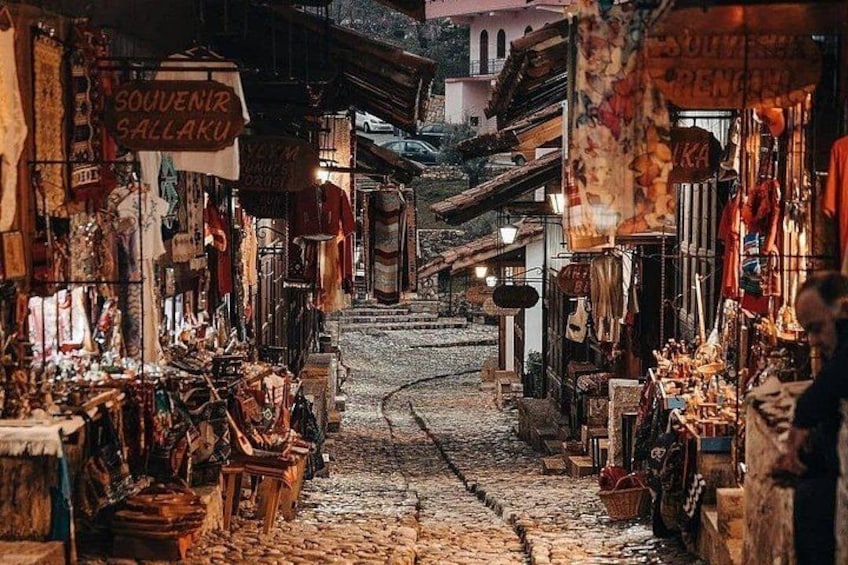 A narrow street with shops on either side, cobblestone pavement, and signs in a foreign language. 1