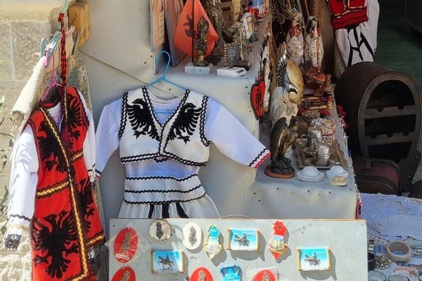 A display of traditional clothing and accessories, including a white dress with black embroidery and a red vest with black patterns. 2