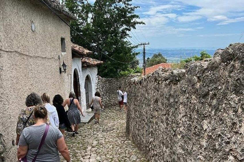 A group of people walking on a cobblestone path beside a stone wall, with a building and trees in the background. 5