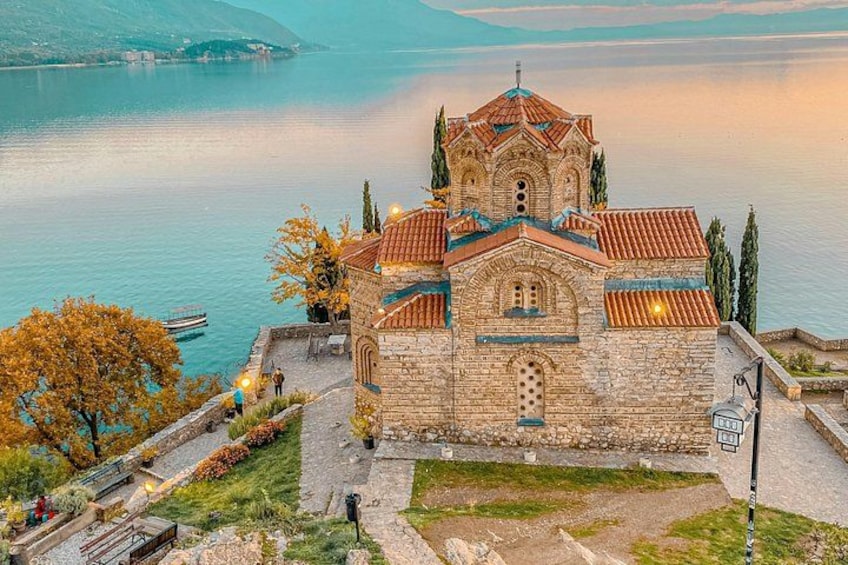 A stone church with a red-tiled roof by a calm lake. 1