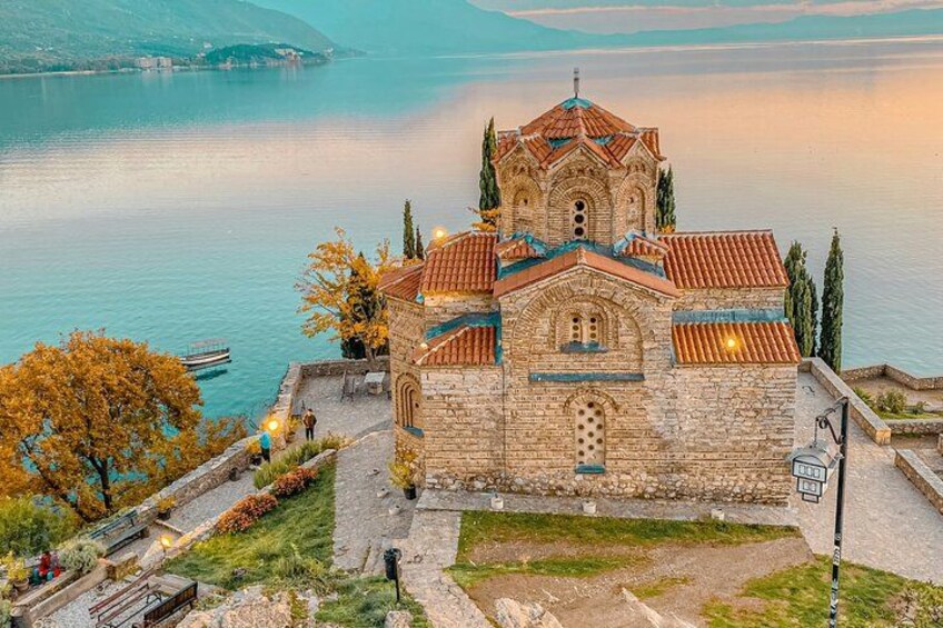 A historic stone church with a red-tiled roof by a lake. 1