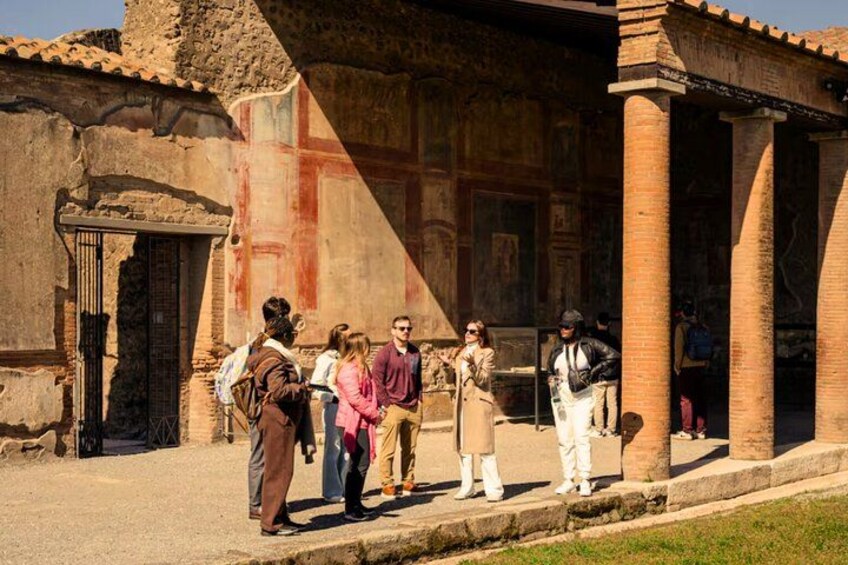 A group of tourists standing in front of an ancient building with columns and a partially visible fresco. 2