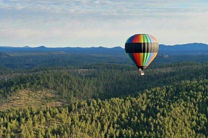 Een luchtballon die boven een bebost landschap met bergen op de achtergrond vliegt. 4