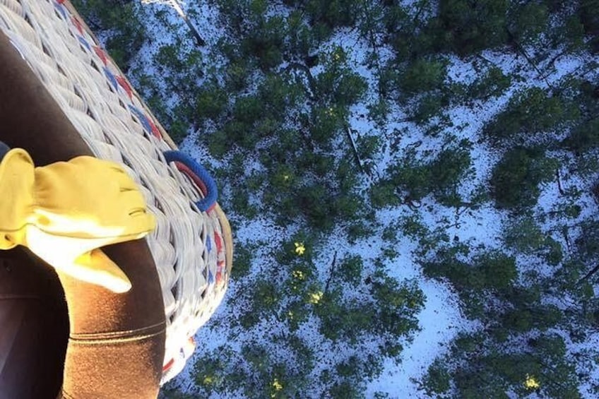 Een persoon met gele handschoenen, een gevlochten mand en een blauw-witte streepzak, met een bebost landschap op de achtergrond. 2