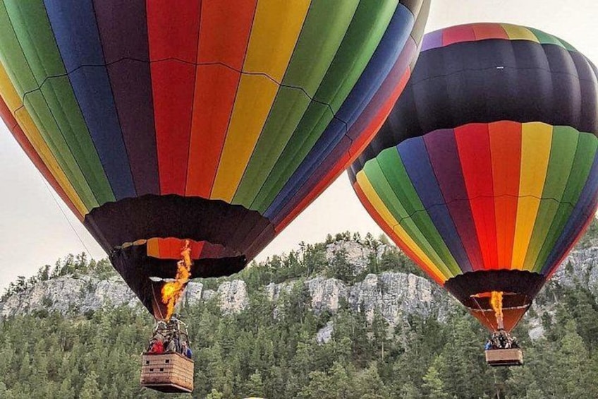 Twee luchtballonnen met kleurrijke strepen vliegen boven een bebost gebied met rotsachtige kliffen. 5