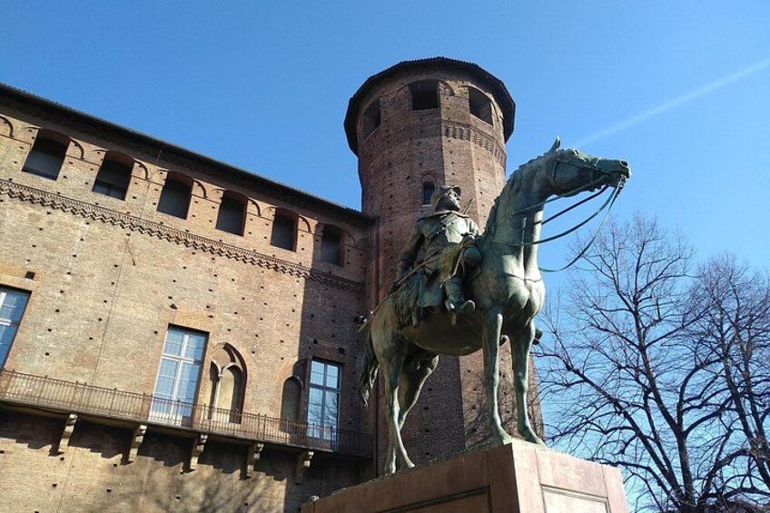 A statue of a man on horseback in front of a brick building with arched windows and a tower. 3
