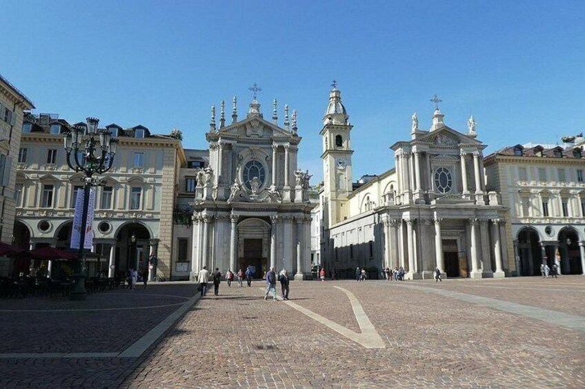 A historic plaza with a prominent church featuring a large clock and bell tower, surrounded by classical architecture. 3