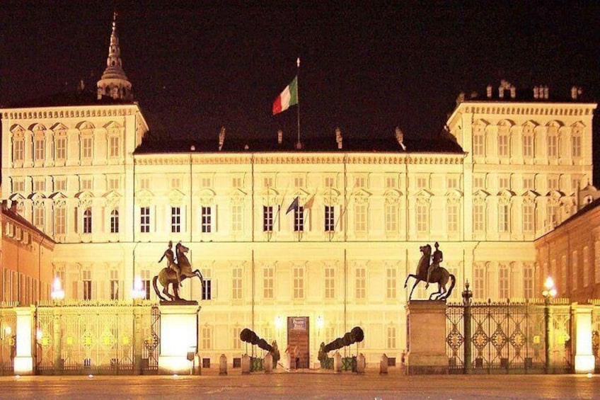 A large, illuminated building with statues of riders on horses, a flag, and a prominent tower. 1