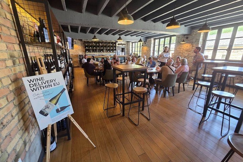 A restaurant interior with wooden floors, brick walls, and hanging lights. There are tables and chairs for dining, and a wine rack with bottles. 5