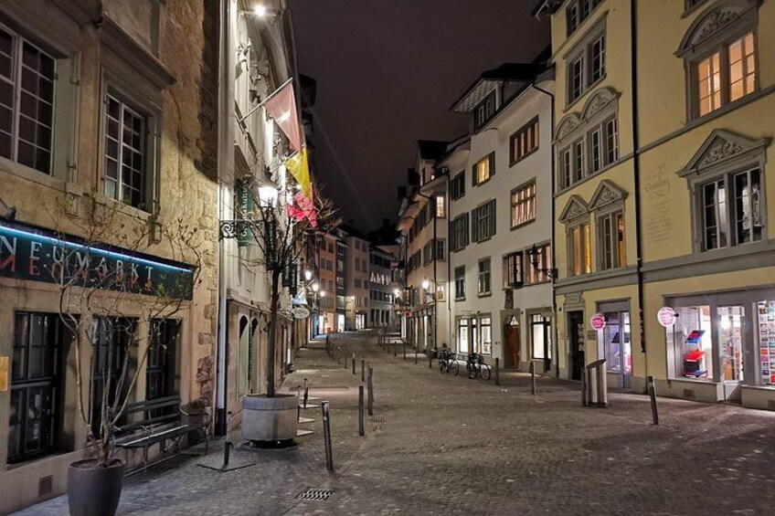 A nighttime street with buildings, a bicycle, and a trash bin. 3