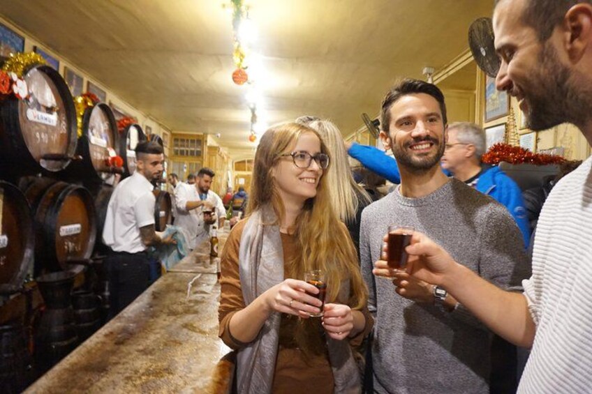A bar with wooden barrels, people holding drinks, and a festive atmosphere. 1