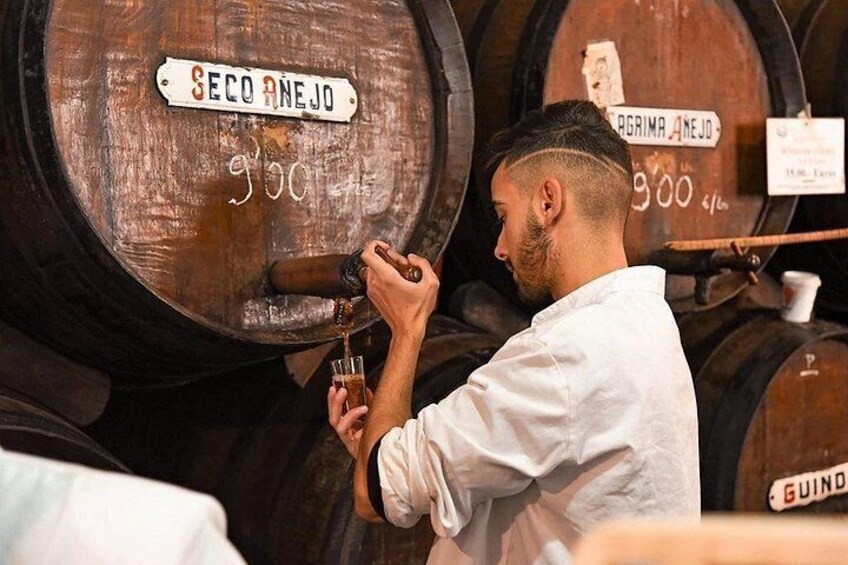 A person pouring a liquid from a barrel labeled 'SECO ANEJO' into a glass. 2