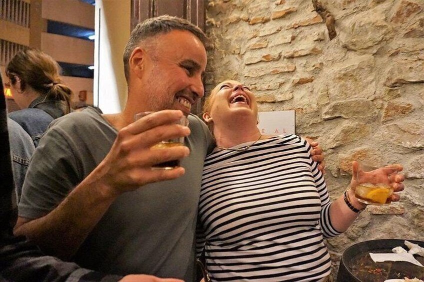 A person holding a glass, another person with a striped shirt, and a stone wall in the background. 5