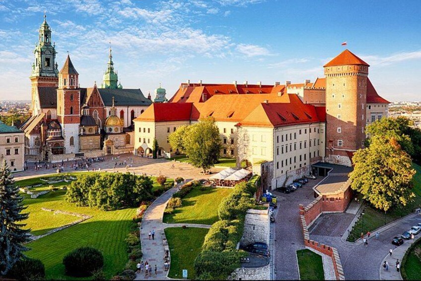 A historic castle complex with a central tower, a church, and a well-maintained garden. 1