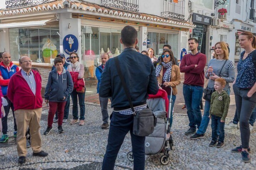 A group of people standing on a cobblestone street in front of a building with a blue sign. 1