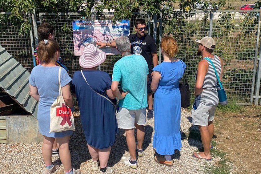A group of people standing in front of a fence, looking at a sign. 2