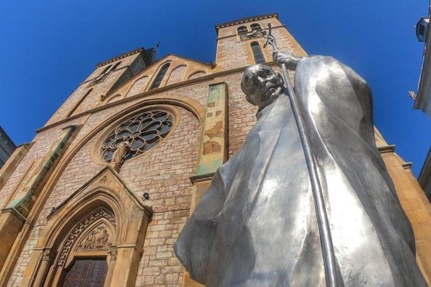 A church with a large statue of a figure holding a staff, a tall bell tower, and a large circular window. 1