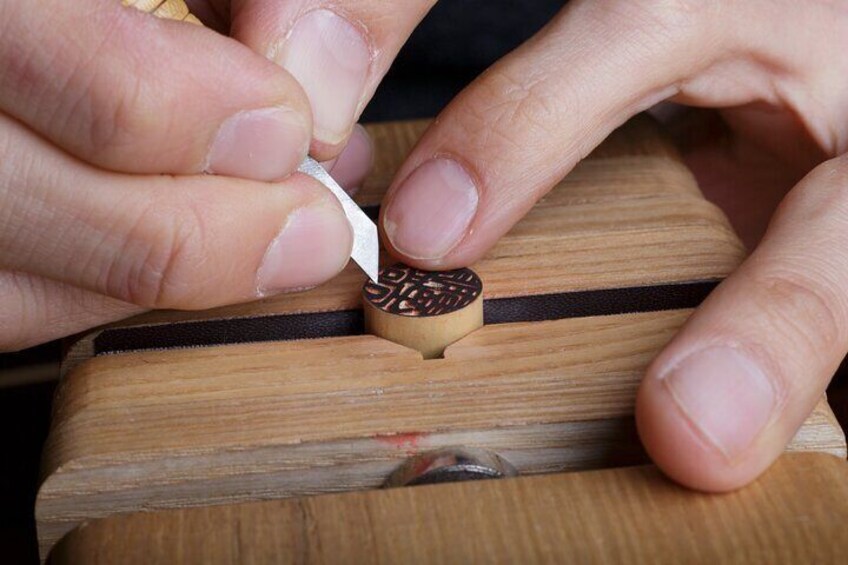 Hands carving a wooden object with a tool. 1