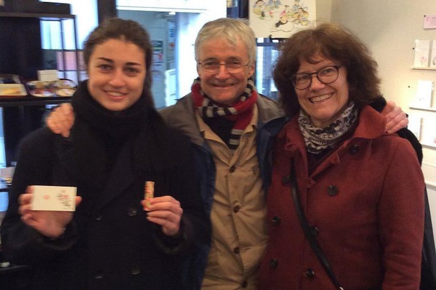 Three people standing indoors, one holding a cup and another holding a book. 2