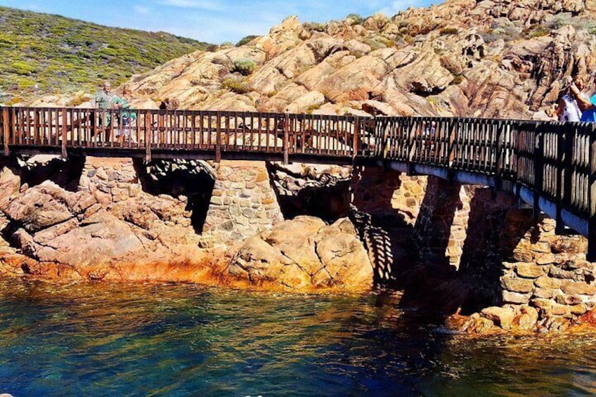 Un puente de madera sobre un lecho rocoso de río, con gente caminando. 3