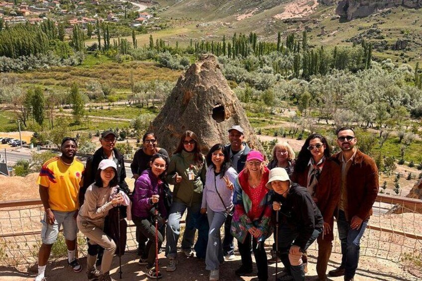 A group of people standing in front of a large rock formation with a mountainous landscape in the background. 2