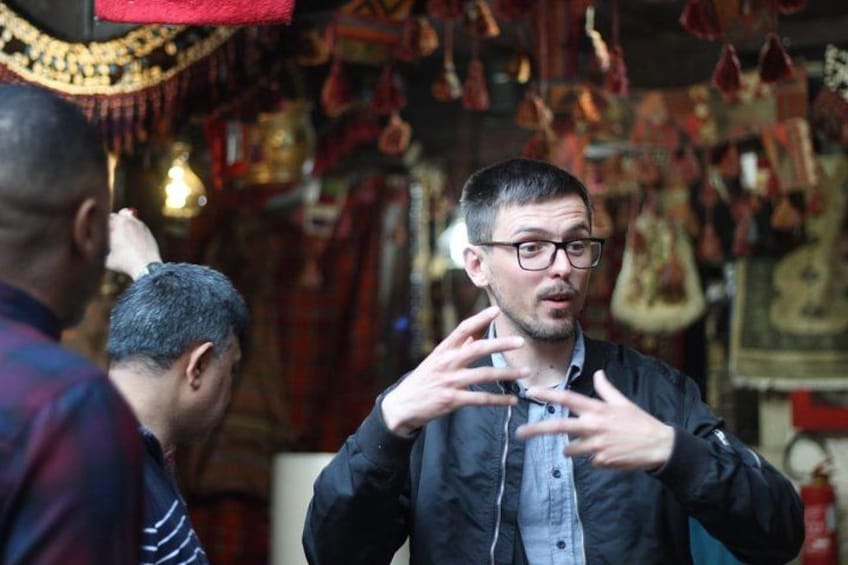 A person in a black jacket with a blue shirt underneath, gesturing with their hands. 2