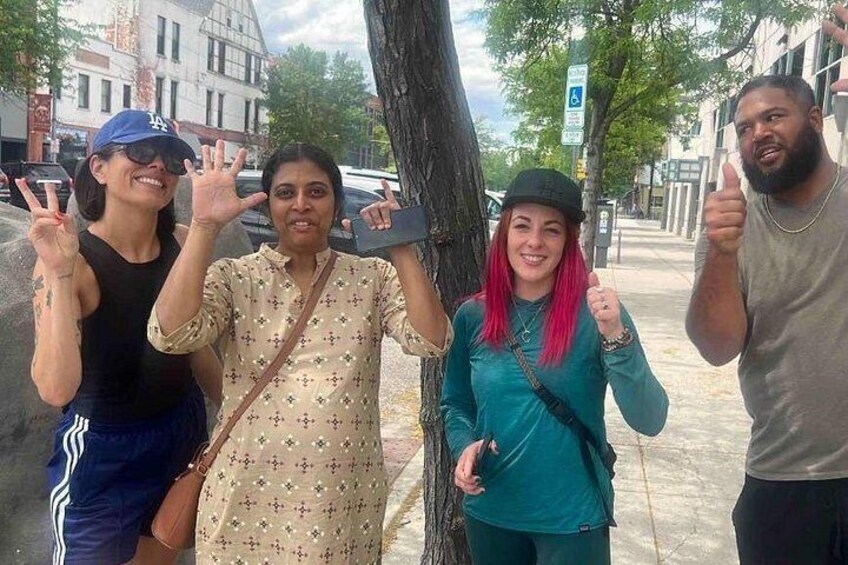 A group of people posing on a sidewalk with a tree and buildings in the background. 3