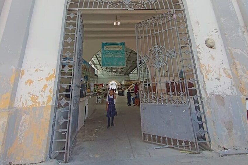 An open metal gate leading into a covered market area with a person standing in the foreground. 2