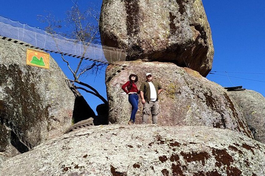 Two people standing on a large rock formation with a mountain range in the background. 3